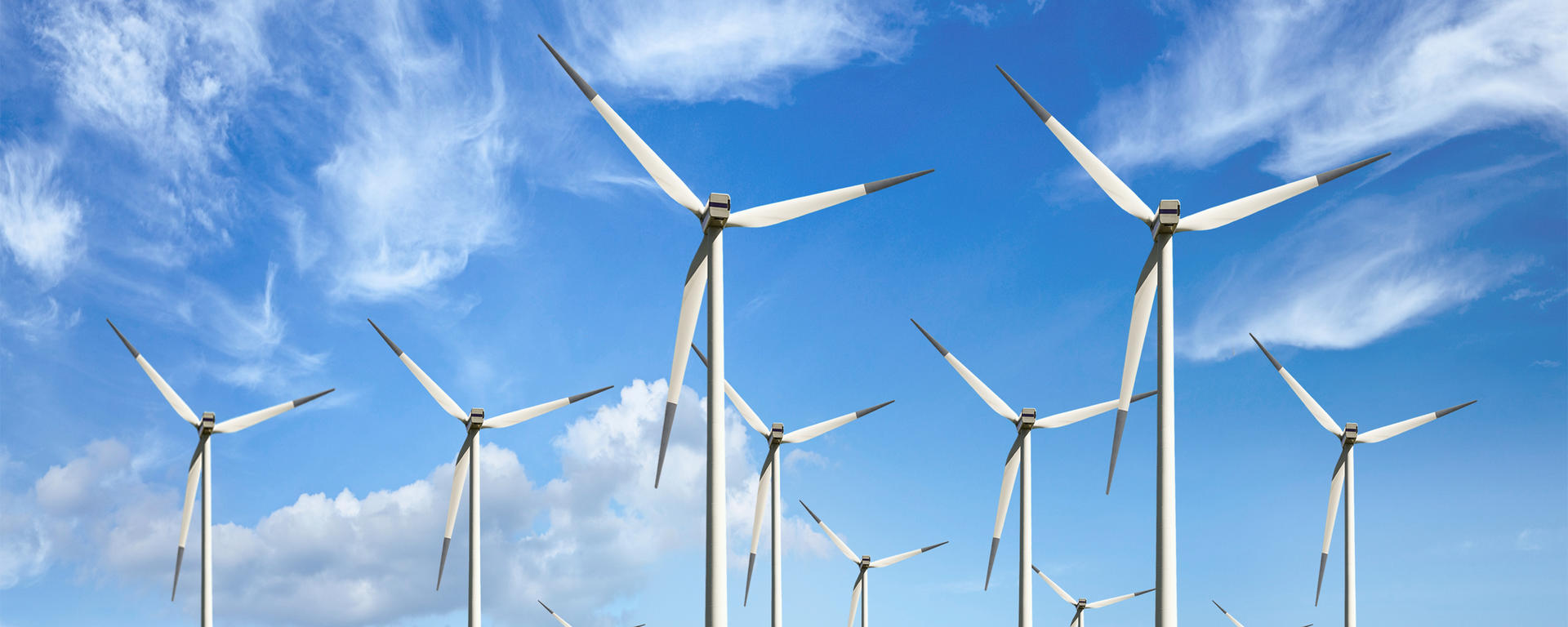 Wind turbines stand against a partly cloudy blue sky